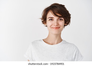 Kopfaufnahme einer schönen Kaukasierin mit kurzen Haarschnitt, Lächeln und selbstbewusst aussehen, im T-Shirt auf weißem Hintergrund stehen.
