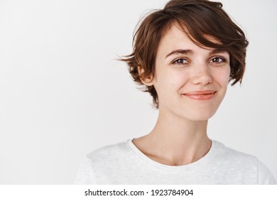 Kopfaufnahme einer schönen natürlichen Frau mit kurzen Haaren, Lächeln und aussehen glücklich, mit T-Shirt, stehend auf weißem Hintergrund.