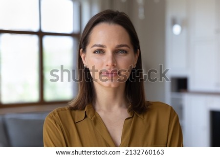 Head shot beautiful young 30s female standing in fashionable living room alone pose looking at camera. Homeowner or apartment renter person, pretty housewife portrait, natural womens beauty concept