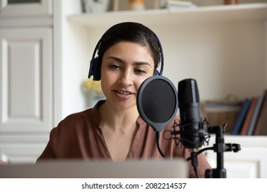 Head Shot Beautiful Young Indian Ethnicity Woman In Headphones Talking In Professional Stand Microphone, Recording Audio For Personal Blog, Singing Song Or Voice Acting Using Computer Applications.