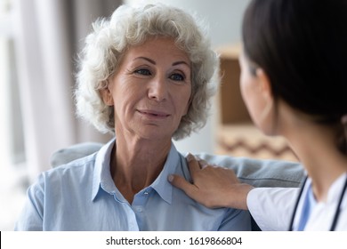 Head shot caring nurse supporting, comforting beautiful older woman with grey curly hair at home, caregiver touching mature patient shoulder close up, healthcare concept, compassion and empathy