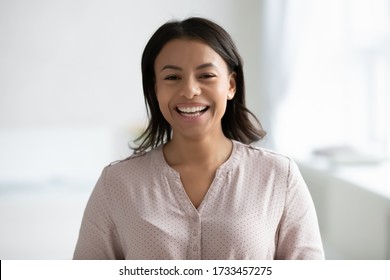 Head Shot Cheerful African Woman With Wide Smile Pose Indoor. Mixed-race Female Blogger Share Positive News Laughing Look At Web Cam Record Video Feels Cheery, Modern Tech, Happy Girl Portrait Concept