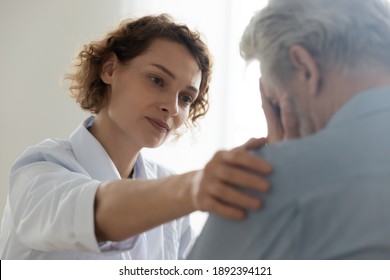 Head shot close up compassionate young general practitioner doctor supporting desperate stressed older mature retired man at appointment. Medical kindness, psychological help, soothing concept.