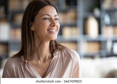 Head shot close up happy attractive businesswoman looking away, feeling excited about new challenges. Smiling pleasant young woman dreaming of future at home, planning workday alone in office.
