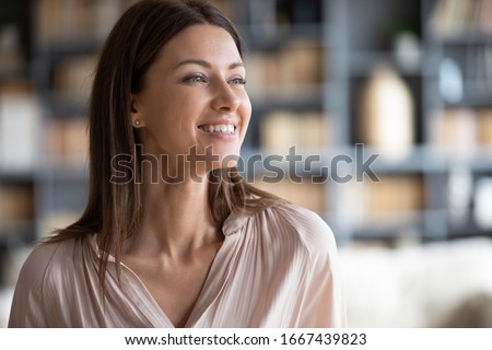 Head shot close up happy attractive businesswoman looking away, feeling excited about new challenges. Smiling pleasant young woman dreaming of future at home, planning workday alone in office.