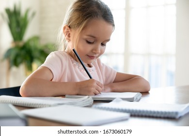 Head Shot Close Up Happy Little Schoolgirl Sitting At Table, Doing Homework. Smiling Smart Small Child Girl Doing Logic Exercises Alone At Home. Children Education, Lessons Preparation Concept.