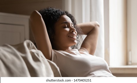 Head shot close up happy smiling mixed race young woman sitting on sofa, crossing hands behind head, relaxing with closed eyes, enjoying quiet lazy day on comfortable sofa in modern living room alone. - Shutterstock ID 1470405251