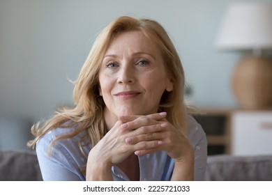 Head shot close up portrait attractive middle-aged woman resting on cozy sofa alone at home staring at camera, posing for photo looks peaceful and confident. Midlife, medical insurance cover for older