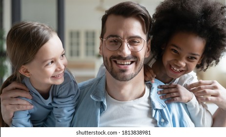 Head shot close up portrait of emotional happy young man playing with laughing small european and african american kids girls at home, smiling multiracial cheerful family having fun together indoors. - Powered by Shutterstock