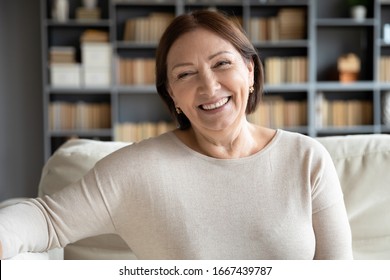 Head shot close up portrait happy healthy middle aged woman sitting on comfortable couch at home. Smiling pleasant 50s elderly mother looking at camera, posing for photo in modern living room. - Powered by Shutterstock