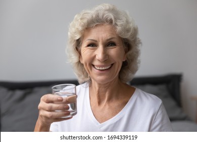 Head shot close up portrait happy senior elderly woman holding glass of fresh pure distilled water, looking at camera. Smiling middle aged grandmother enjoying healthy habit, drinking aqua every day. - Powered by Shutterstock