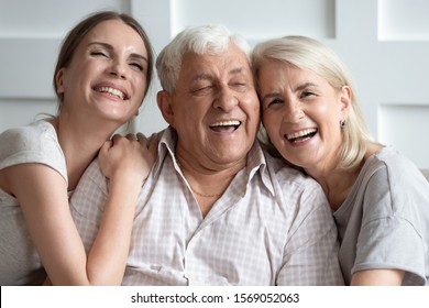 Head Shot Close Up Portrait Overjoyed Attractive Young Woman Having Fun With Happy Older Parents. Laughing Two Generations Enjoying Free Leisure Family Time Together At Home, Posing For Photo.