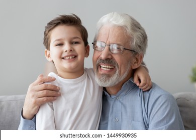 Head Shot Close Up Portrait Smiling Grandfather Wearing Glasses Hugging Cute Little Grandson, Looking At Camera, Happy Grandparent And Preschool Grandchild Posing For Family Photo At Home Together