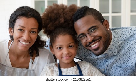 Head Shot Close Up Portrait Of Smiling African Ethnicity Parents Posing For Photo With Adorable Small Preschool Kid Girl Indoors, Happy Couple Enjoying Cooking Time With Cute Child Daughter In Kitchen