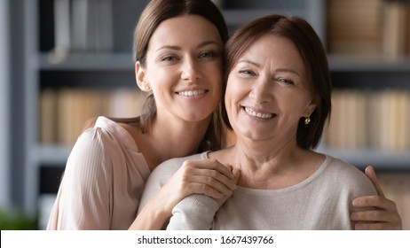 Head Shot Close Up Portrait Young Affectionate Woman Cuddling Older Senior Mother, Posing For Photo At Home. Happy Loving Two Generations Women Family Looking At Camera, Enjoying Time Together.