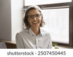 Head shot close up profile picture of beautiful middle-aged businesslady posing in workplace, smiling, look at camera, feel satisfied with career growth and success. Business portrait, professionalism