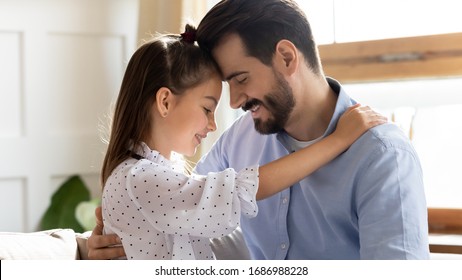 Head shot close up side view affectionate little child daughter touching foreheads with smiling bearded father. Happy small kid girl enjoying sweet moment with dad in living room, trustful relations.