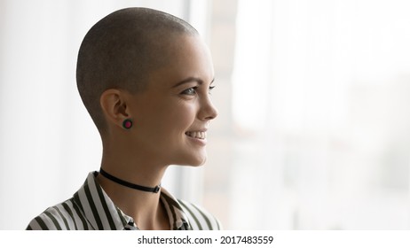 Head shot close up side view pretty woman with shaved bald head looking out of window in distance, dreaming contemplating cityscape. Inspired young hairless lady feeling inspiration, defeating cancer. - Powered by Shutterstock