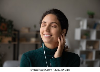 Head shot close up smiling woman enjoying popular music with closed eyes, good quality sound, wearing using earphones, satisfied attractive young female listening to favorite song, relaxing - Shutterstock ID 2021404316