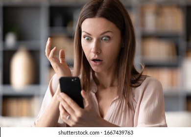 Head shot close up young shocked woman looking at mobile phone screen, received bank debt notification. Stunned frustrated lady reading sms with unbelievable news on smartphone, making big eyes.