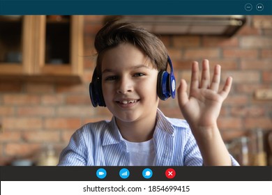 Head shot cute happy small schoolboy in headphones looking at web camera, greeting classmates or teacher at online study lesson, enjoying distant e-learning education at home, computer screen view.