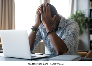 Head shot desperate millennial mixed race man holding head in hands, feeling exhausted after long computer work. Tired frustrated young biracial businessman suffering from financial problems.