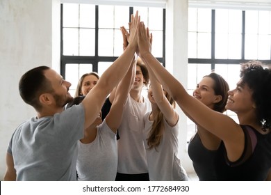 Head Shot Excited Young Mixed Race Sporty People Joining Hands In Air, Giving High Five To Each Other, Celebrating Team Success Or Self Supporting Before Intensive Workout In Modern Sport Club.