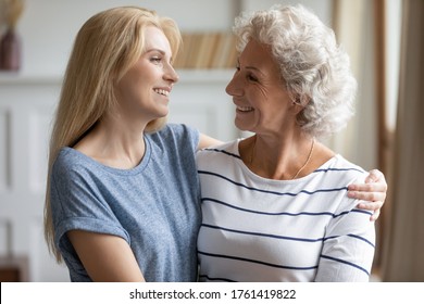 Head shot grown up granddaughter and elderly grandmother hugging smiling looking at each other standing indoors feeling love, having warm relations, understanding between multi-generational family