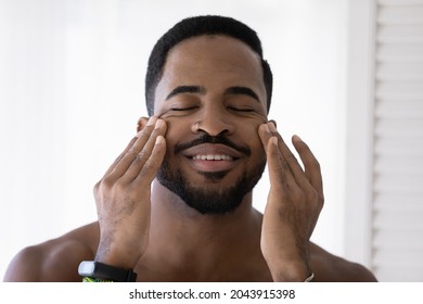 Head shot handsome African man touch face massages smooth perfect skin, applying day or night facial cream enjoy quality cosmetics. Self-care, skincare, personal hygiene for beauty and health concept