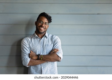 Head Shot Of Handsome Young African American Guy, Young Black Man With Dreads Wearing Casual Stylish Shirt, Glasses, Keeping Hands Folded, Smiling At Camera. Male Portrait With Copy Space