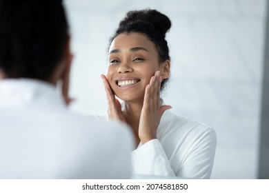 Head shot happy beautiful young african american woman in white bathrobe touching face, feeling satisfied with moisturized healthy skin condition after morning spa treatment procedures in bathroom. - Powered by Shutterstock