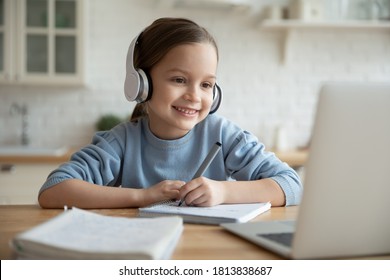 Head Shot Happy Cute Little 7s Old Kid Girl Wearing Earphones, Looking In Laptop Screen, Involved In Online Foreign Language Private Lesson With Tutor Or Enjoying Distant E-learning School Class.