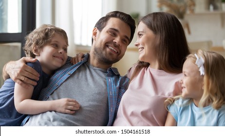 Head shot happy family couple looking at each others eyes, hugging smiling kids. Joyful young parents bonding embracing little cute siblings children, enjoying spending weekend time together at home.