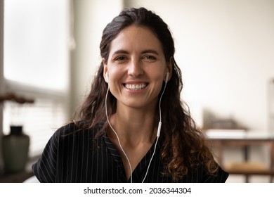 Head shot of happy Latin woman with wire earphones looking at camera, talking, speaking, smiling at webcam. Video call portrait screen view portrait of pretty blogger, coach, teacher giving training