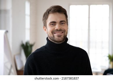 Head Shot Of Happy Male Millennial Posing In White Interior. Profile Picture Of Confident Young Man In Black Casual Sweater Looking At Camera And Smiling. Job Candidate Or Employee Corporate