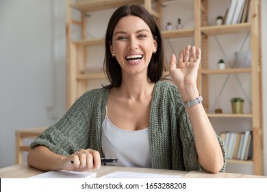 Head shot happy young 30s woman sitting at wooden desk, looking at camera, waving hello. Excited businesswoman teacher lecturer recording educational video, greeting students at online workshop. - Shutterstock ID 1653288208