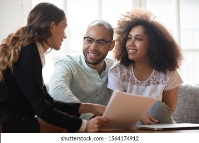 Head shot happy young african american family couple meeting pleasant mixed race real estate agent at home. Smiling married spouse listening to female lawyer, financial advisor, broker propose.