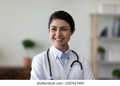 Head Shot Happy Young Female Indian GP Doctor Therapist In White Medical Coat Looking In Distance, Thinking Of Career Opportunities Or Professional Challenges, Feeling Confident At Workplace.