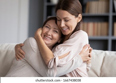 Head shot happy young woman hugging excited old senior mother, glad to hear good news. Smiling grownup daughter embracing pleasant kind middle aged mommy, resting on comfortable sofa at home.