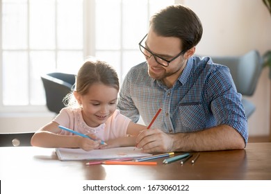 Head shot joyful young dad drawing pictures in paper album and happy small daughter  enjoying free leisure time at home  Smiling little kid girl learning painting and father  sitting at table 