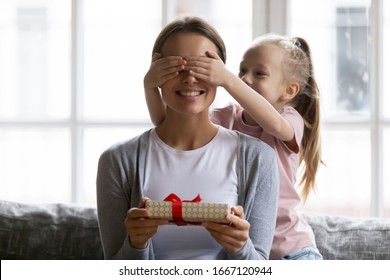 Head shot little blonde school aged girl covering eyes of curious young mother, preparing secret gift. Excited small kid daughter congratulating smiling mommy with birthday international woman day.