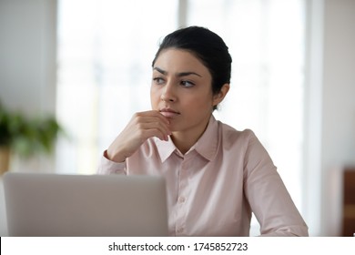 Head Shot Lost In Thoughts Young Indian Woman Sitting In Front Of Computer, Looking Away. Thoughtful Millennial Professional Solving Problems, Finding Inspiration, Thinking Over Hard Decision.