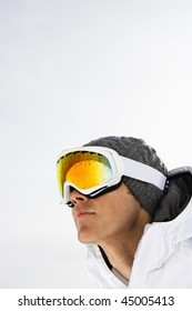 Head Shot Of A Male Skier Wearing Ski Goggles Against A Snowy White Background. Vertical Shot.