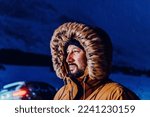 Head shot of a man in a cold snowy area wearing a thick brown winter jacket, snow goggles and gloves on a cold Scandinavian night. Life in the cold regions of the country.