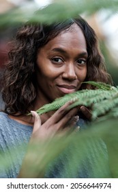 Head Shot Of Mature Black Woman Touching A Plant And Looking To Camera.