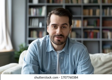 Head shot millennial guy sit on sofa in living room makes video call looks at camera, conversation by distant videocall, distance hiring job interview process, tutor and trainee study on-line concept
