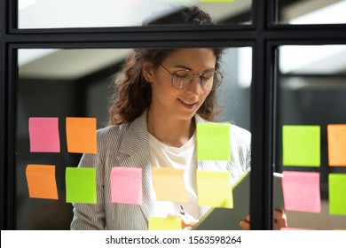Head shot motivated smiling pleasant smart businesswoman in eyeglasses checking start up project progress, using kanban agile scrum method glass board and digital tablet software at modern office. - Shutterstock ID 1563598264