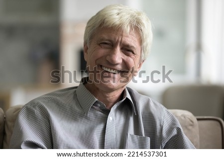Head shot of optimistic aged man sit on sofa staring at camera feel happy looking satisfied spend time alone at home enjoy carefree life on retirement. Medical insurance, dental services for elderly
