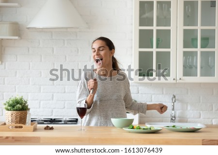 Head shot overjoyed young mixed race woman holding whisk, pretending to be singer, singer favorite pop song while cooking at modern kitchen. Happy lady having fun, cooking breakfast alone at home.