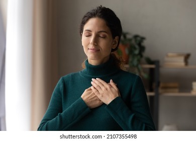 Head shot peaceful young attractive woman holding folded hands on chest, praying waiting for miracle, feeling thankful indoors. Sincere happy female volunteer showing kindness or expressing gratitude. - Shutterstock ID 2107355498
